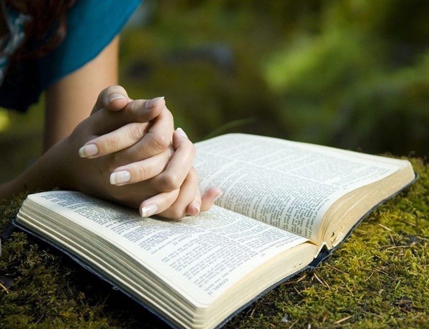 St. John's United Church | A person with clasped hands rests on an open book in a natural setting.