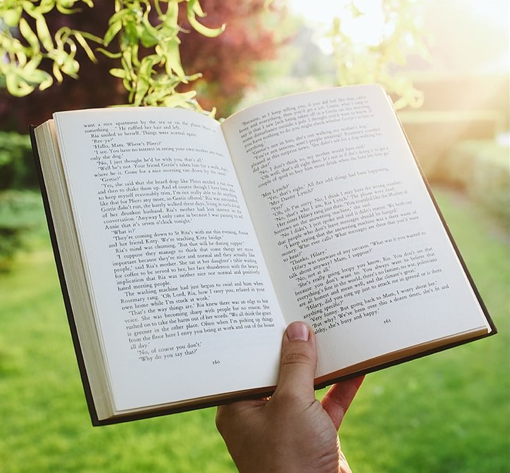 St. John's United Church | Person holding an open book in a sunlit garden, with text visible on the pages.