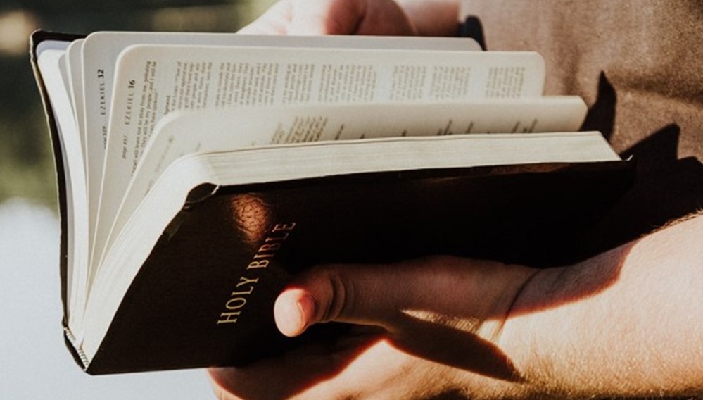 St. John's United Church | Close-up of a person holding an open holy bible, focusing on the book and part of the person's hands.