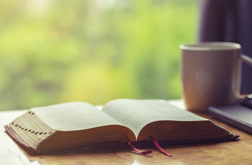 St. John's United Church | Open book on a desk with a cup of coffee and blurred green background.