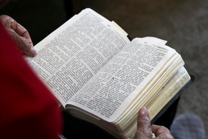 St. John's United Church | An individual is reading an open book with dense text, possibly a Bible, while holding the pages.
