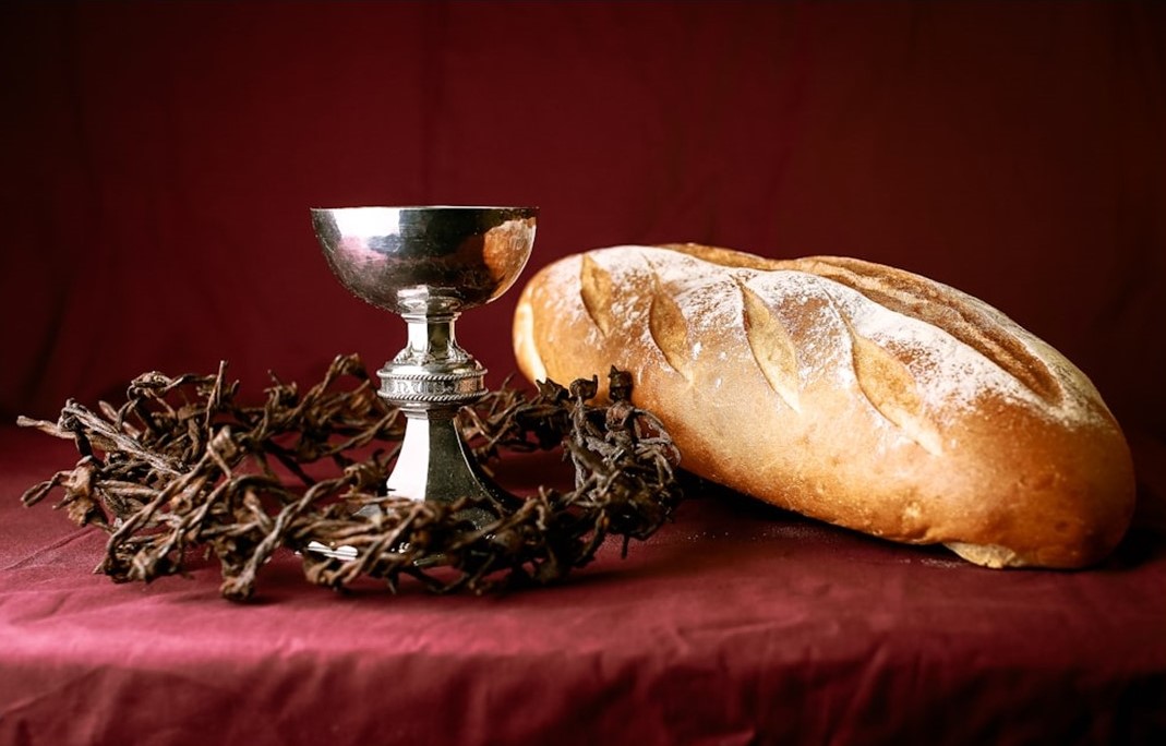 St. John's United Church | A loaf of bread, a silver chalice, and a crown of thorns are placed on a red cloth backdrop.