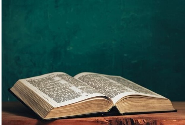 St. John's United Church | An open book with black and white text lies on a wooden surface against a dark green background.