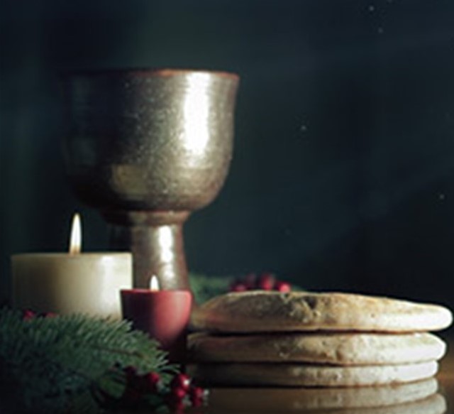 St. John's United Church | A chalice and stack of flatbread are surrounded by lit candles and greenery on a dark background.