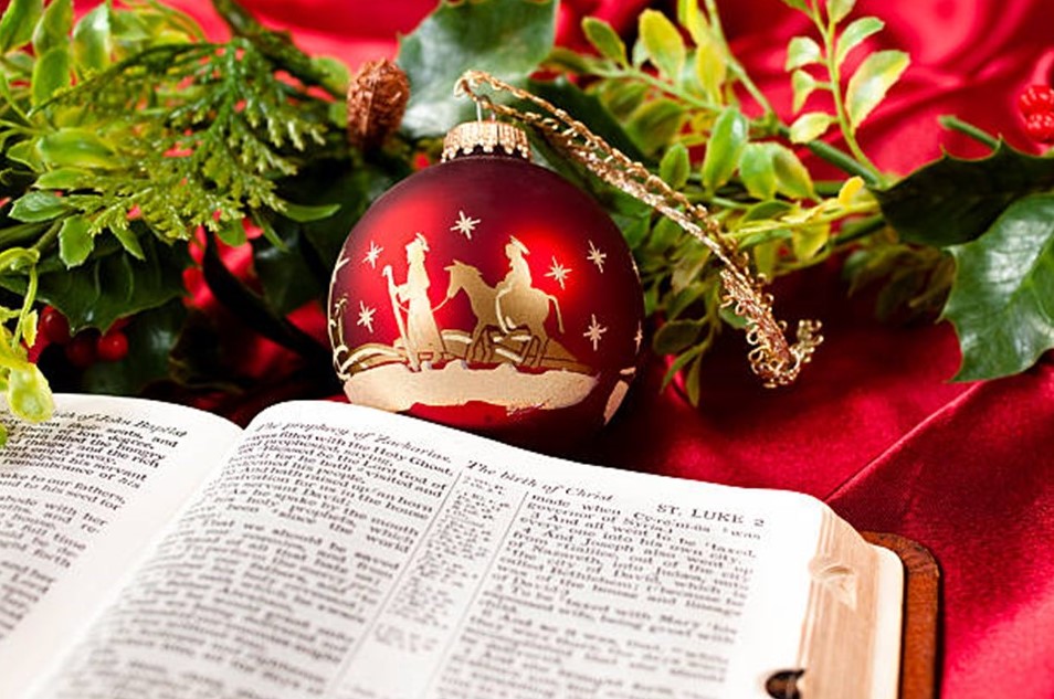 St. John's United Church | A Bible open to Luke 2 lies on a red cloth beside a Christmas ornament depicting a nativity scene, with holly and greenery in the background.