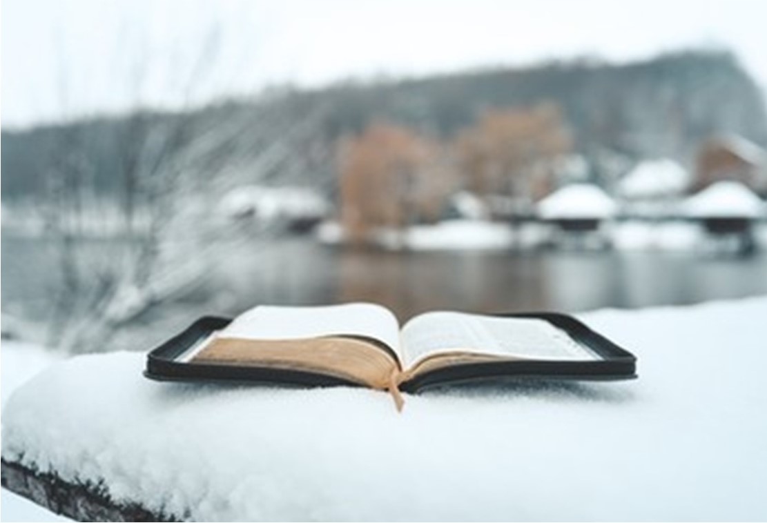 St. John's United Church | An open book lies on a snow-covered surface with a blurred snowy landscape and lake in the background.