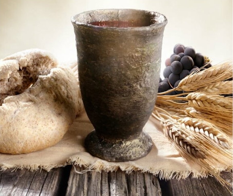 St. John's United Church | A rustic chalice on a wooden table, accompanied by a loaf of bread, a bunch of grapes, and wheat stalks.