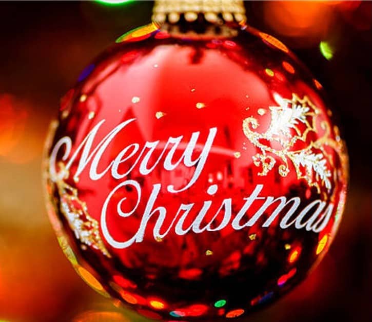 St. John's United Church | A close-up of a red Christmas ornament with "Merry Christmas" written in white script and decorative gold accents, hanging on a tree.