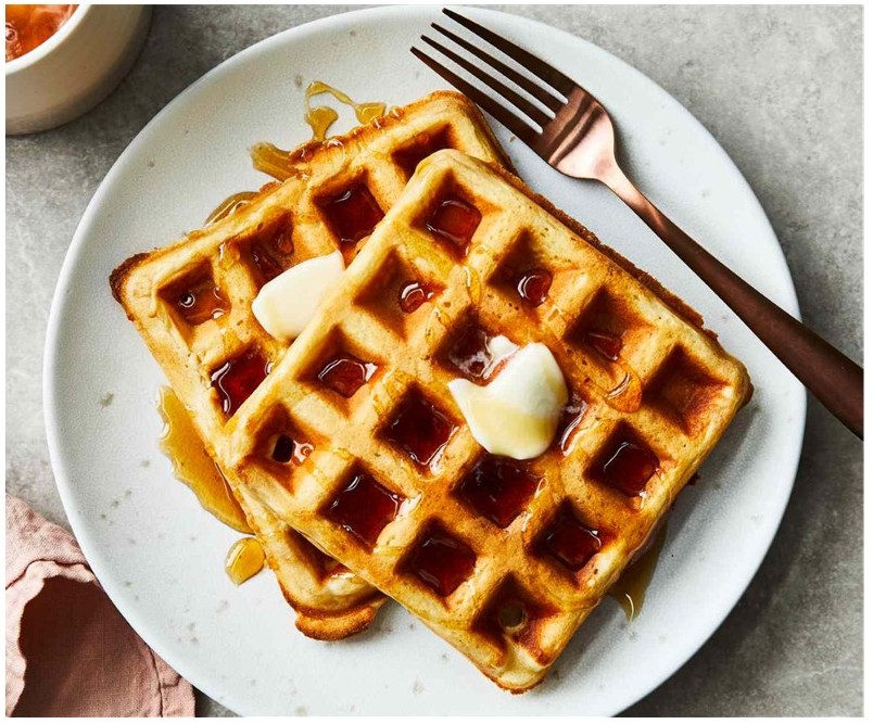 St. John's United Church | Two golden waffles topped with butter and syrup on a white plate, with a fork placed beside them.
